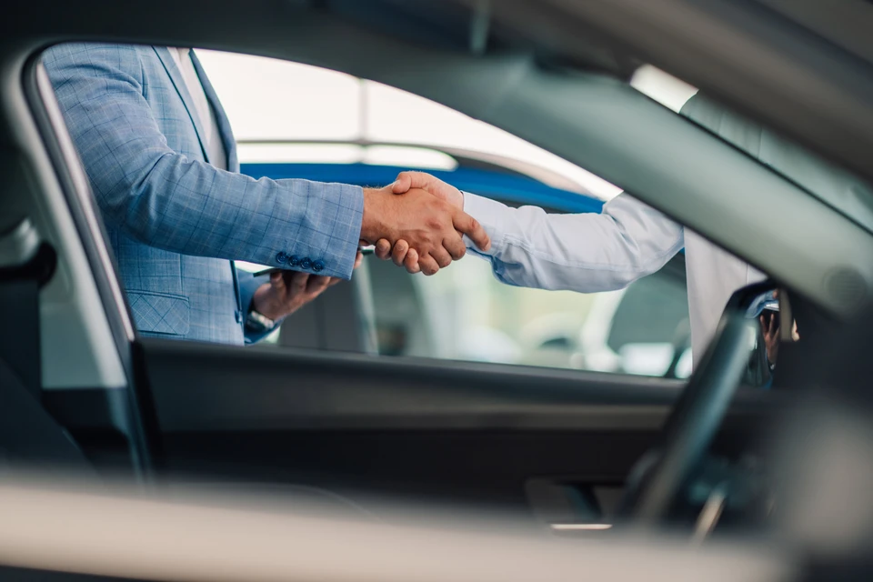 Une poignée de main finale et l'échange de clés de voiture entre deux individus, l'un portant un costume bleu et l'autre en chemise blanche, symbolisant la conclusion réussie d'une transaction chez un concessionnaire automobile